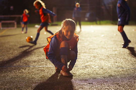 Portrait smiling girl soccer player tying shoe on field at night