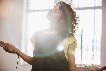 Carefree young female dancer listening to music with headphones and mp3 player in sunny studio