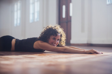 Smiling, carefree young female dancer stretching on dance studio floor