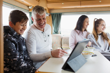 Family relaxing, eating breakfast and using digital tablet in motor home