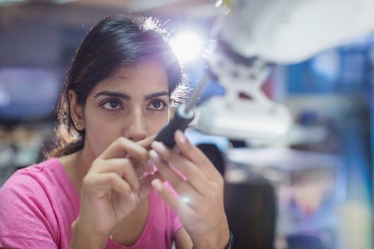 Focused female engineer with screwdriver fixing robotic arm