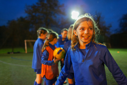 Smiling girl playing soccer on field at night