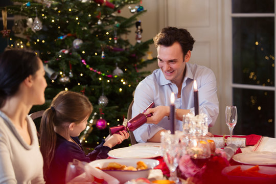 Father and daughter pulling Christmas cracker at candlelight dinner table