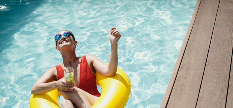 Carefree woman with inflatable ring drinking cocktail in sunny swimming pool