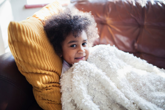Portrait cute girl relaxing, cuddling on sofa with blanket and pillow