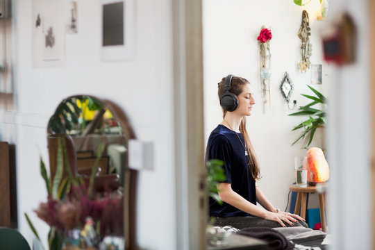 Serene young woman meditating with headphones in apartment