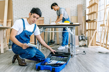 Carpenter doing his job in carpentry workshop. Portrait of adult carpenter teaching apprentice standing at table in workshop, copy space.