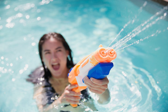 Playful woman using squirt gun in sunny summer swimming pool