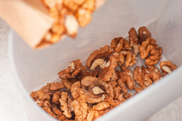 Pouring walnuts from a paper bag into a plastic storage container.