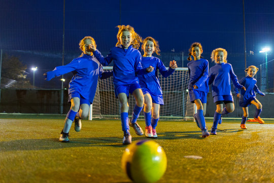 Girls soccer team playing, running toward ball on field at night