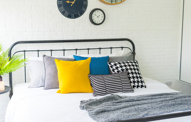 yellow and blue pillows on bed in modern bedroom with many clock on wall.