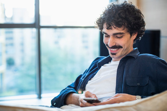 Smiling Man Using Smart Phone On Sofa