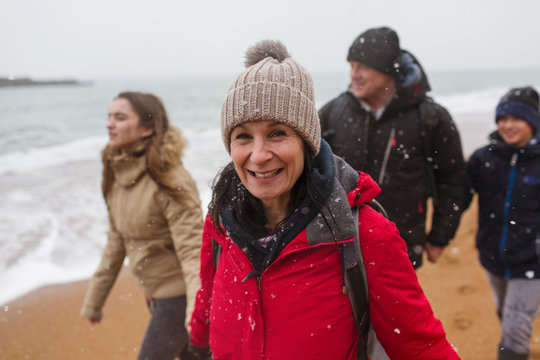 Portrait smiling woman in warm clothing with family on snowy winter ocean beach