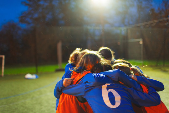Girls soccer team huddling on field at night