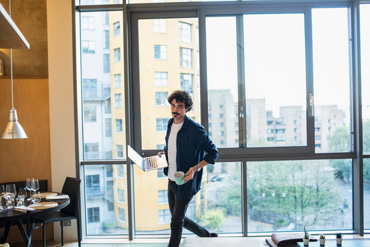 Man with laptop and coffee walking in urban apartment