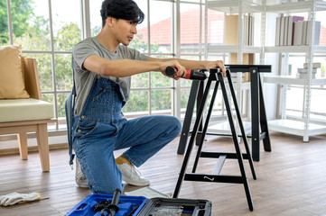 Bearded joiner in safety glasses drills an electric drill hole in a wooden Board in the home workshop