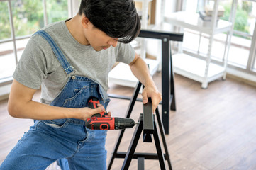 Bearded joiner in safety glasses drills an electric drill hole in a wooden Board in the home workshop