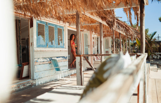 Woman in bikini standing in doorway of sunny beach hut