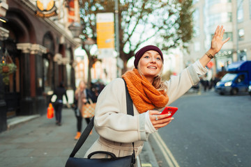 Woman with smart phone hailing taxi on urban street