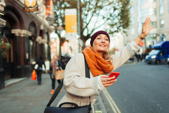 Woman With Smart Phone Hailing Taxi On Urban Street