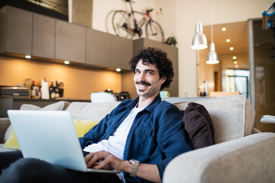 Portrait smiling man using laptop on apartment sofa