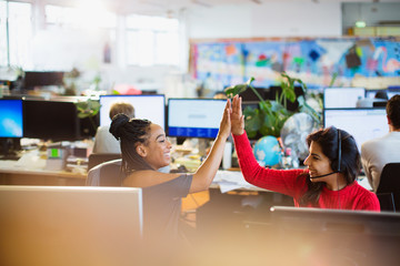 Happy businesswomen high-fiving at computers in open plan office