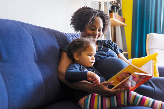 Pregnant mother and daughter reading book on sofa