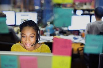 Businesswoman with headset working at computer behind adhesive notes