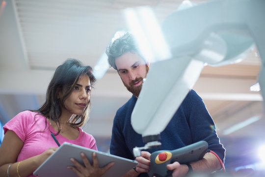 Engineers with digital tablet programming robotic arm in office