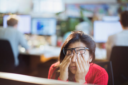 Tired, stressed businesswoman rubbing eyes in office