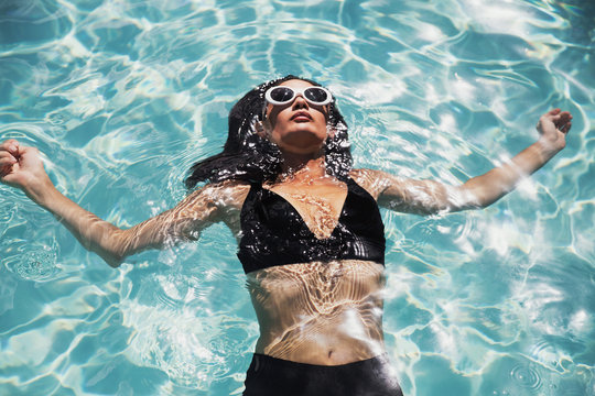 Serene woman in black bikini floating in sunny summer swimming pool