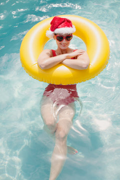 Portrait smiling woman in Santa hat and heart-shape sunglasses swimming with inflatable ring in swimming pool