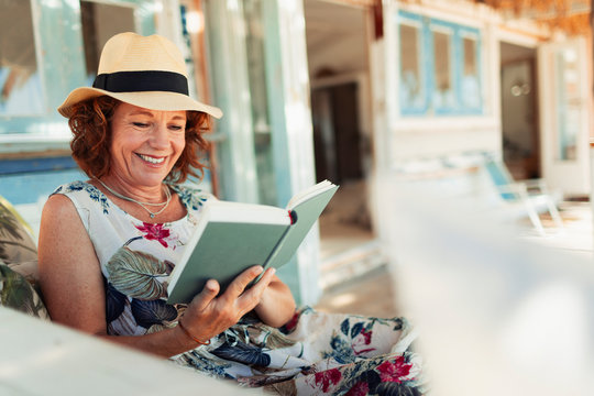 Happy woman reading book on beach hut patio