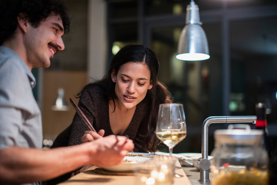 Couple eating dinner with chopsticks and drinking white wine in apartment kitchen