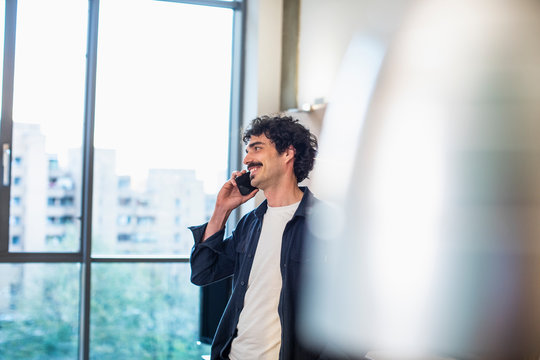 Smiling man talking on smart phone at urban apartment window