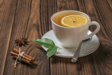 A Cup of fresh tea with lemon and cinnamon on a wooden table in the sun.