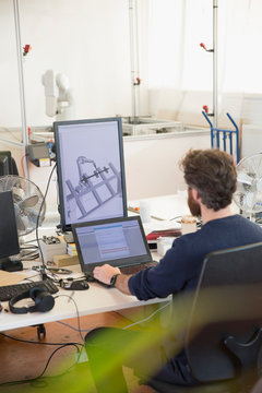 Male engineer programming robotics, working at laptop in office