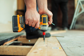 Close up construction worker using power drill installing floorboard