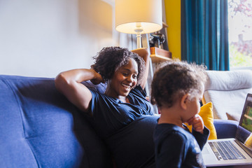 Happy pregnant mother and daughter using laptop on sofa