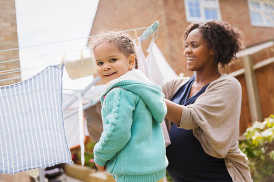 Portrait happy girl helping pregnant mother hang laundry on clothesline