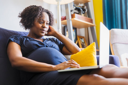 Pregnant woman using laptop on sofa