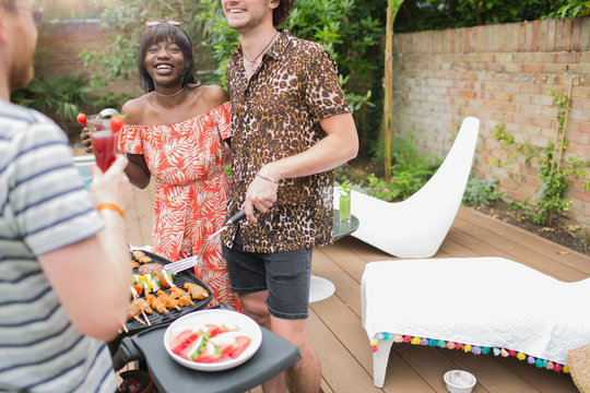 Happy young multiethnic couple barbecuing on summer patio