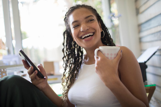 Portrait happy young woman with smart phone and tea laughing