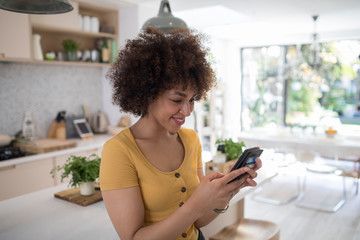 Smiling young woman using smart phone in kitchen