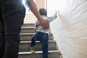Father helping toddler son climb stairs in stairwell