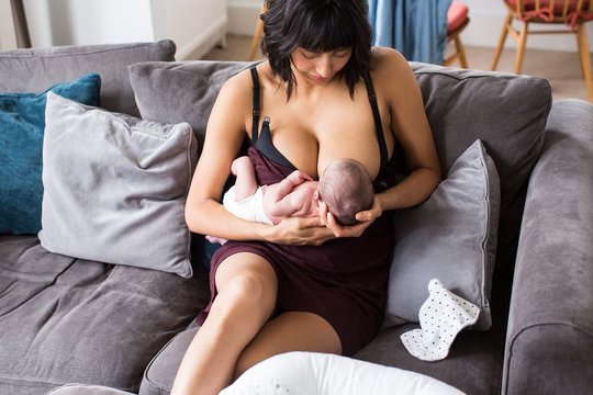 Mother breastfeeding newborn baby son on sofa