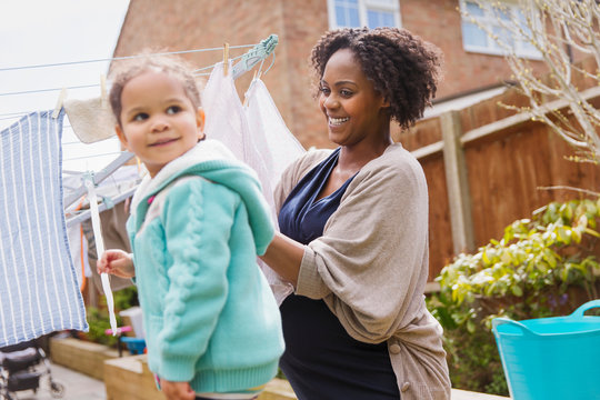 Happy pregnant woman and daughter hanging laundry on clothesline
