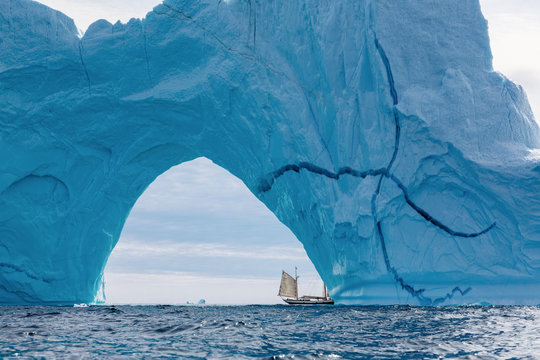 Sailboat under majestic iceberg arch Atlantic Ocean Greenland