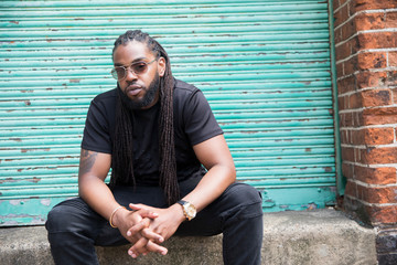 Portrait confident cool man with long braids in urban alley