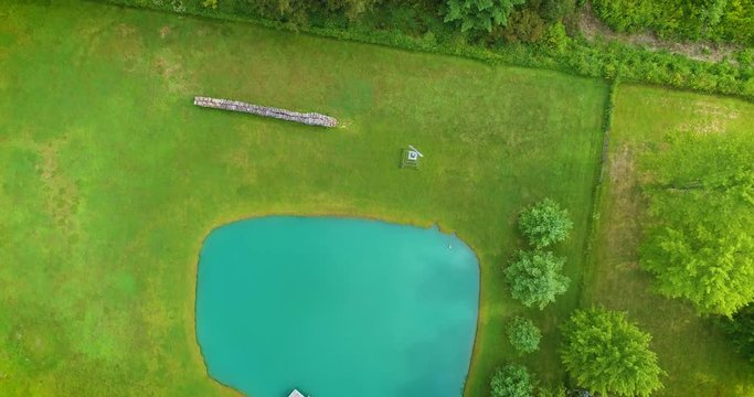 Aerial top-down drone footage of a blue pond and trees in the country.